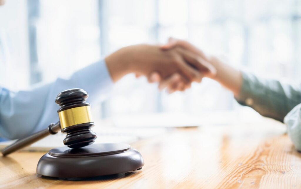 Two blurry people shaking hands in background with a gavel in the foreground